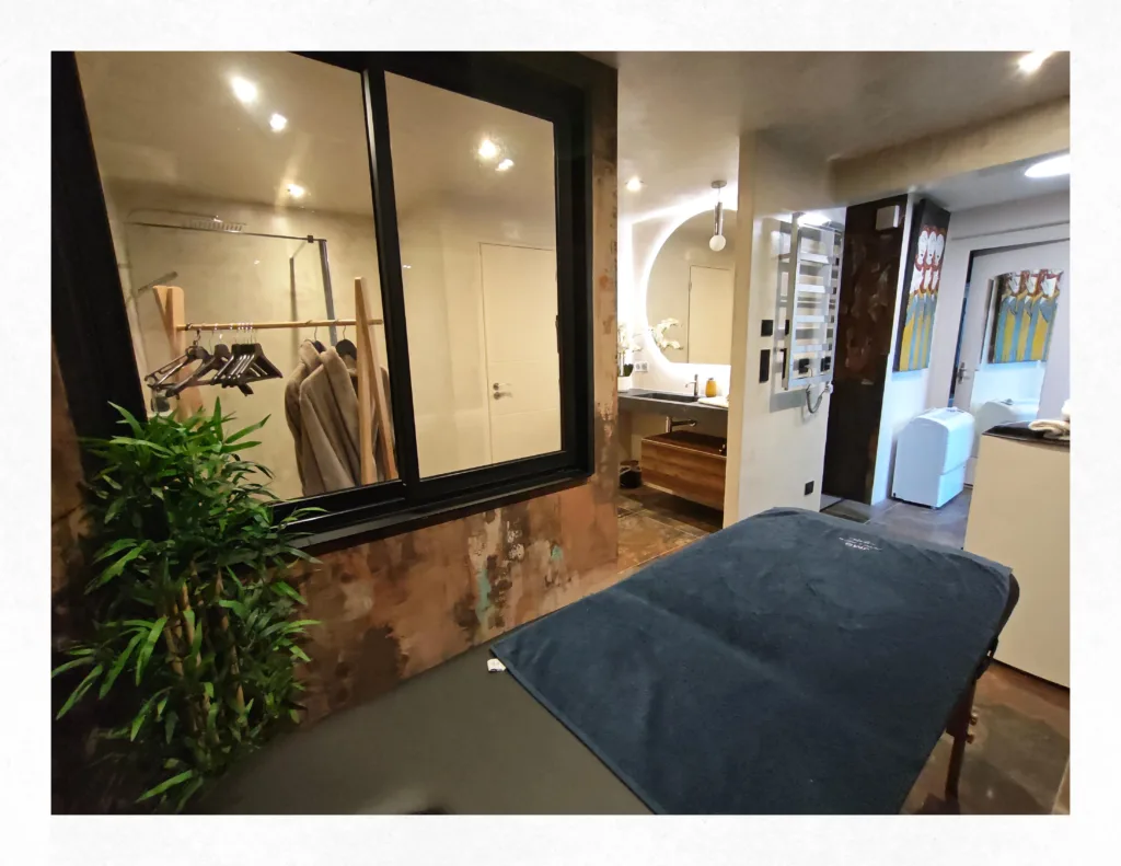 Table de massage dans la suite Ananda avec murs et plafonds en béton ciré, jouxtant l'espace salle de bain haut de gamme à Carnac.