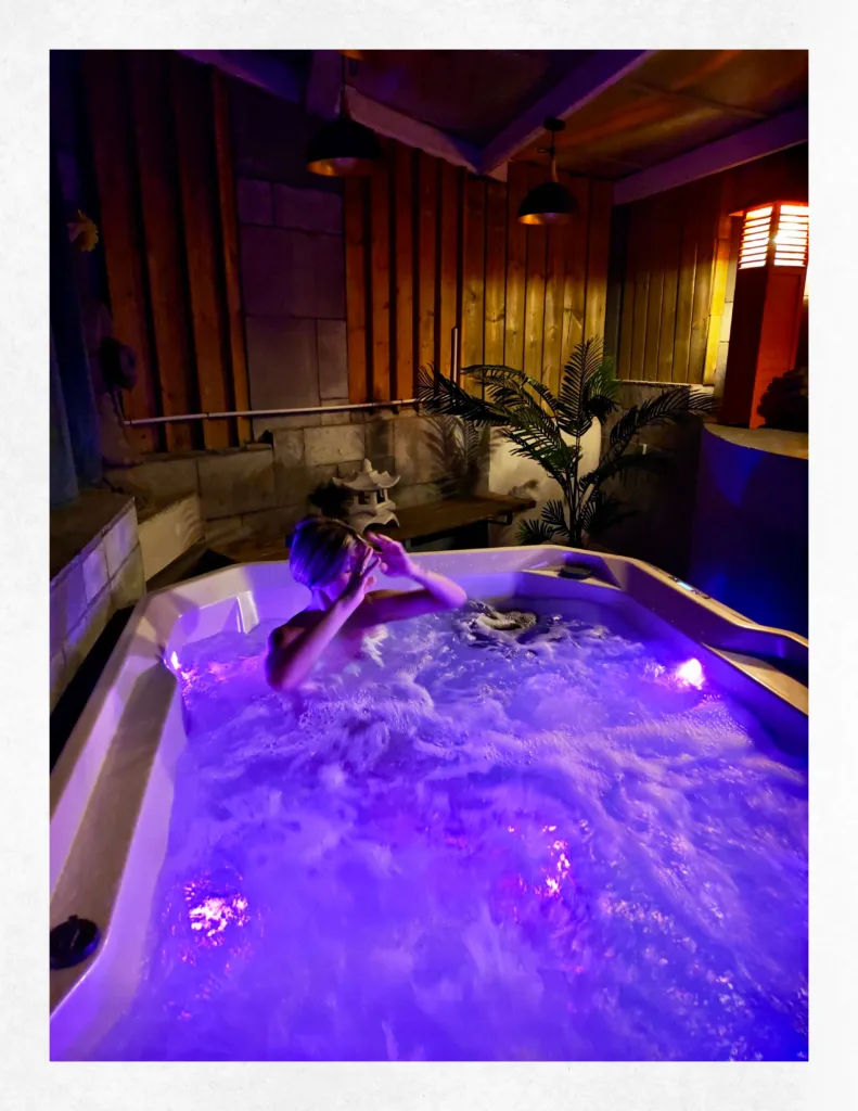 Femme se relaxant dans l'eau bouillonnante illuminée en violet du jacuzzi sous le patio en bois de la Suite Ananda.