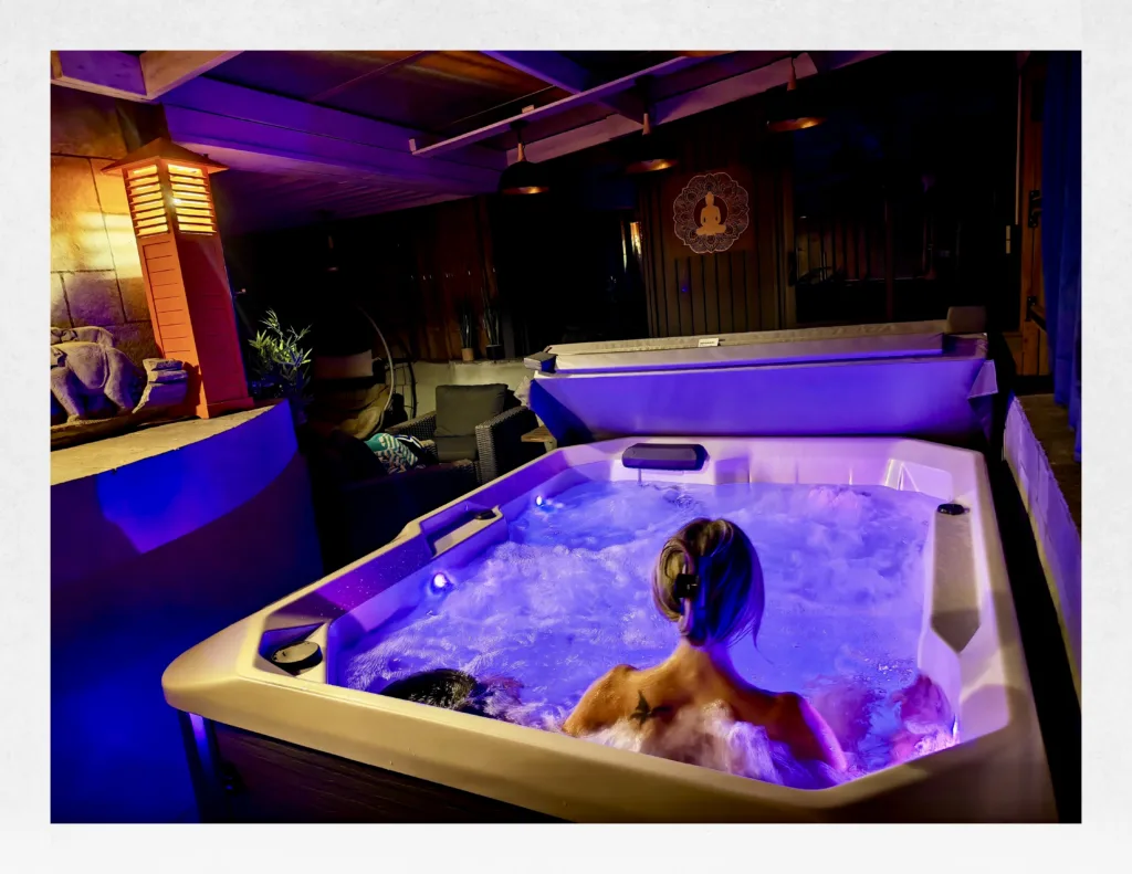 Espace spa avec lumières led violettes et jacuzzi privatif en marche sous le patio couvert de la suite Ananda.