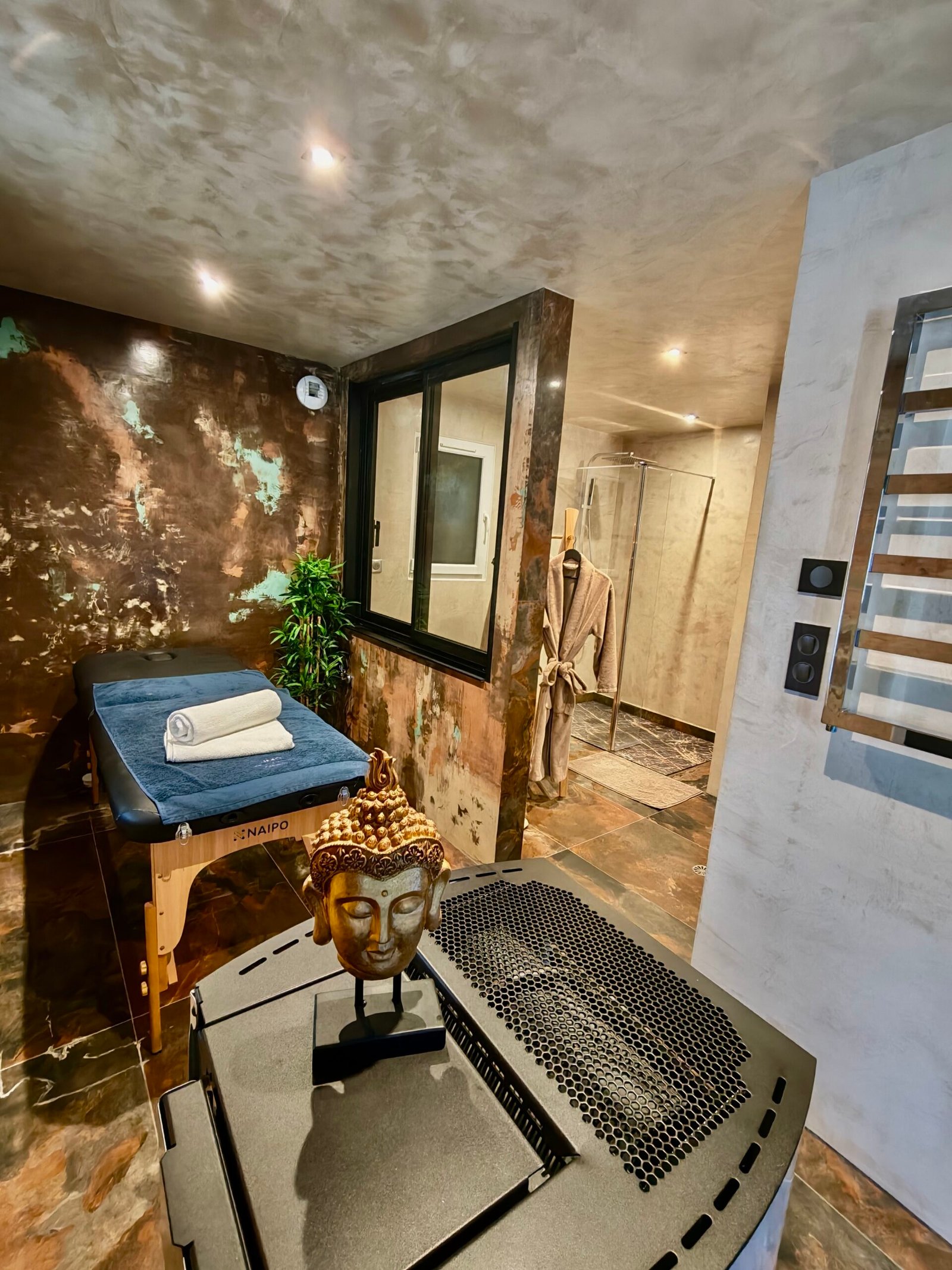 Espace soin avec table de massage professionnelle Naipo, poêle à pellets et décoration zen en béton ciré dans la suite Ananda à Carnac
