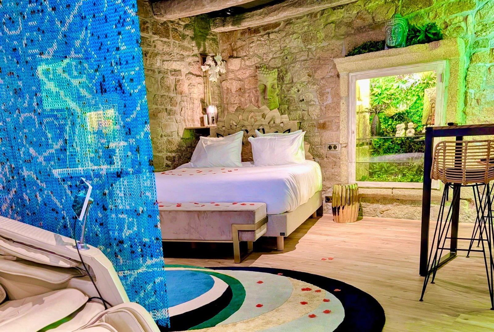 Chambre romantique de la Suite Samadhi avec lit King Size, murs en pierre apparente et vue sur le mur végétal aux Suites du Bouddha Bleu à Carnac